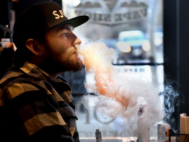 Social pot use: Initiative 300 would create a four-year pilot program allowing regular businesses, such as bars or cafes or even yoga studios, to seek permits for bring-your-own marijuana, over-21 consumption areas that are indoors or outdoors. Pictured: Jon Ferrar, sales associate, exhales from his vaporizer at Boulder Vapor House on November 17, 2014. (Mark Leffingwell, Daily Camera)