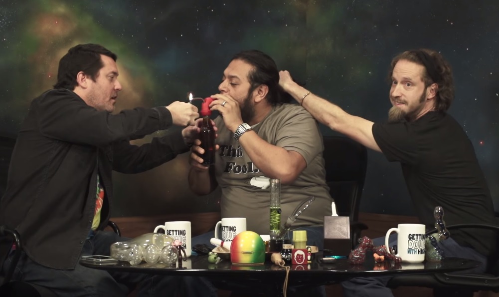 "Getting Doug with High" host Doug Benson (left) lights a bottle-pipe for Felipe Esparza while Josh Blue pulls back his hair. (Screen cap courtesy of Jash)
