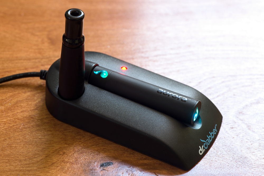 A photo of the Dr. Dabber Aurora in its charging station, on a wooden desk.